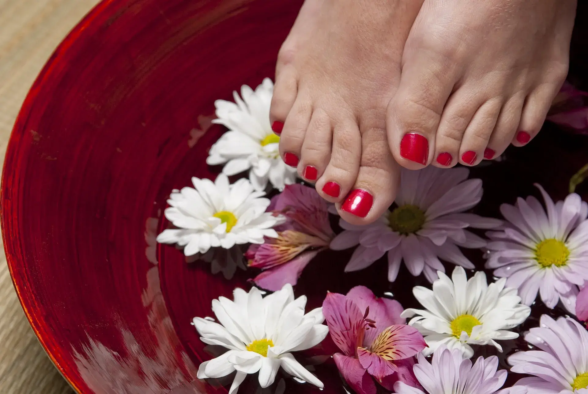 Crveno lakirani nokti na nogama iznad posude sa vodom i cvijećem